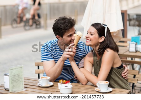 Young couple enjoying coffee at a street cafe laughing as they share an ice cream cone in the hot summer sun