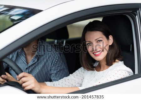 Beautiful competent female driver looking out of the window of the car with a lovely warm smile as she drives along with a male passenger