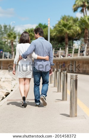 Loving couple walking away arm in arm along a beachfront promenade as they enjoy a vacation at the seaside