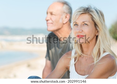 Thoughtful middle-aged woman relaxing at the sea sitting alongside her husband looking up into the sky with a contemplative expression