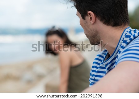 Young man flirting on the beach making eyes at a nearby attractive woman with focus to the side of his head