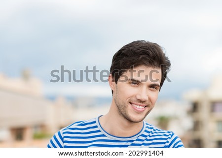 Head and shoulders portrait of a smiling handsome unshaven young man in a striped t-shirt in summer sunshine