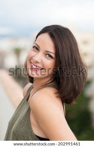 Smiling relaxed beautiful woman with a lovely natural smile posing outdoors turning to look at the camera