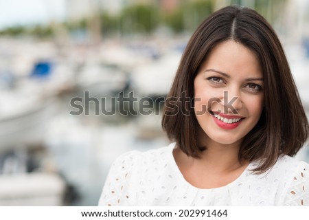 Beautiful friendly young woman with shoulder length brown hair posing outdoors looking directly at the camera with a gentle smile