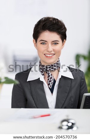 Beautiful elegant hotel receptionist with a lovely friendly smile in a stylish outfit with a scarf and a short modern haircut
