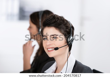 Beautiful friendly call center operator wearing a headset sitting looking up into the air as she listens to the conversation with a client with a smile
