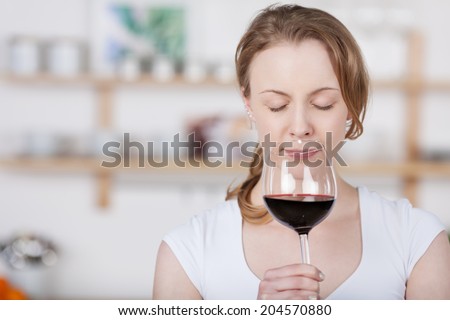 Young woman savoring the bouquet of a glass of wine as she sniffs at the glass with her eyes closed in bliss as she concentrates on the smell, with copyspace indoors in the kitchen