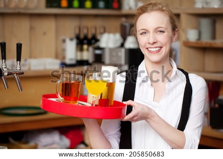 Portrait of confident young waitress carrying tray with coffee; juice and beer in restaurant
