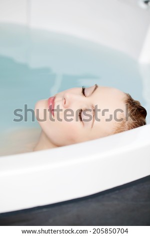 Serene woman relaxing in a round spa bath with her head resting above water with her eyes closed in bliss