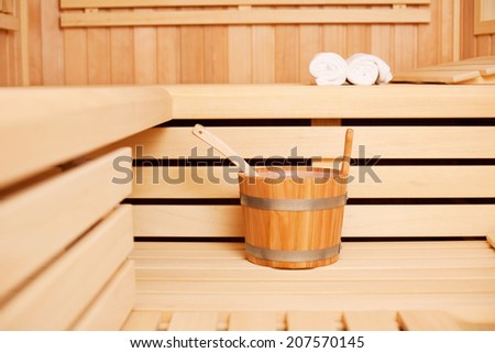 Wooden bucket of water and a ladle in a traditional wooden sauna for pouring onto the heated coals or heat source to produce steam