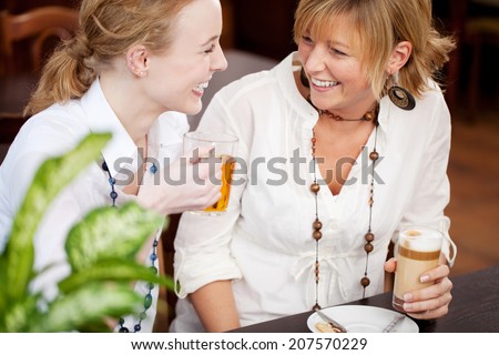 Two women laughing in a restaurant as they sit together at a table enjoying a glass of tea and coffee together