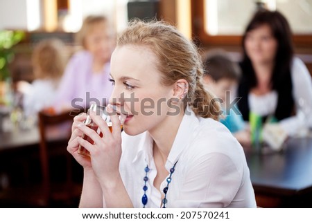 Thoughtful woman enjoying tea in a restaurant sitting at a table cradling the mug in her hands and watching something off screen with a pensive look