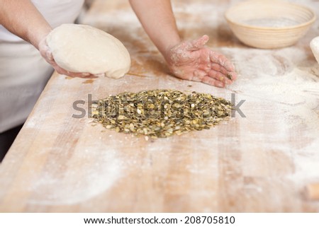 Midsection of male bakery chef holding dough covered with seeds at kitchen counter