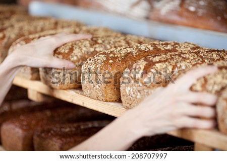 Cropped image of female bakery hands displaying bread loaf from shelves
