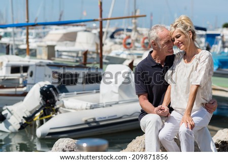 Affectionate couple relaxing in a small boat harbour with the wife sitting on her husbands lap as they nuzzle lovingly