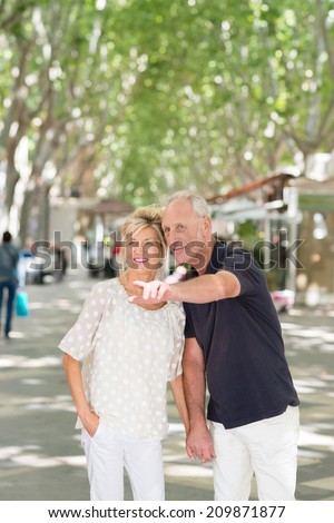 Attractive middle-aged man pointing out something to his wife as they stand close together peering into the distance in a tree lined urban street