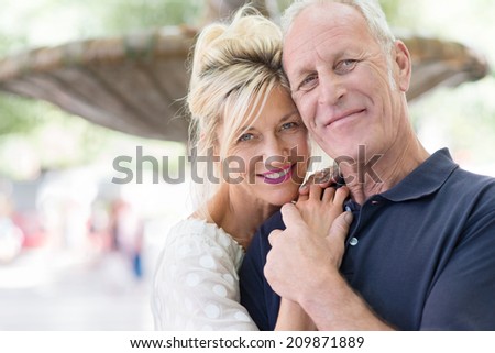 Attractive romantic middle-aged couple posing for their portrait with the heads close together and clasped hands in front of a fountain