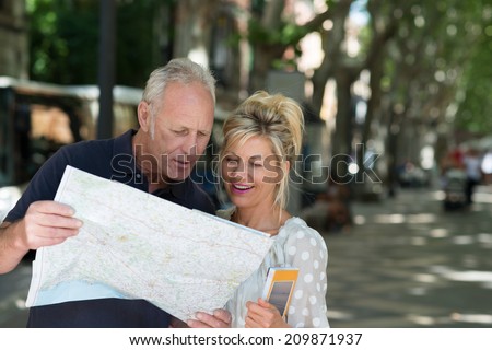Middle-aged tourists consulting a map as they stand in a shady tree lined urban street looking for a specific travel destination