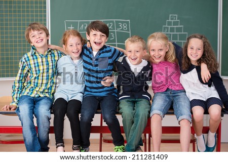 Laughing group of young friends in class sitting in a row in front of the chalkboard grinning happily at the camera