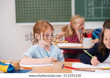 Young girl on class looking at a classmates work as they sit side by side at a desk with a serious expression of concentration