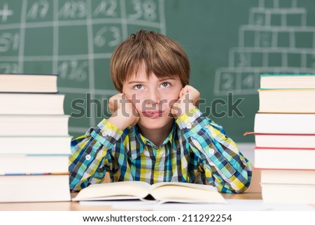 Grumpy little boy in class sitting between two stacks of text books staring morosely up into the air