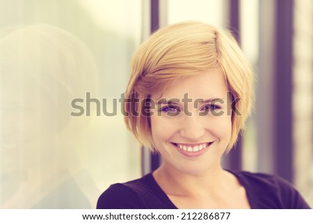 Retro effect portrait of a smiling young woman with short blond hair standing alongside an angled wall with copyspace
