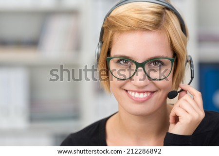 Smiling friendly client services assistant wearing a headset listening to a client discussing a problem while looking at the camera