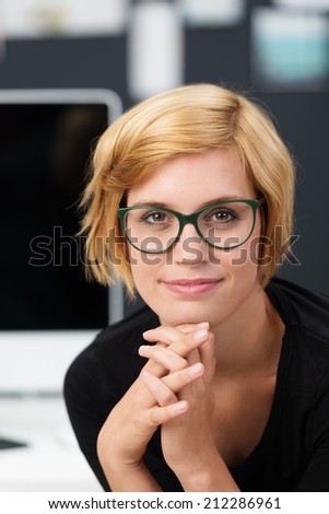 Attractive young woman wearing glasses resting her chin on her hand looking into the camera with a thoughtful smile