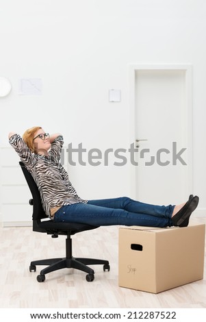 Woman relaxing in her new home or office sitting in an office chair with her feet up on a cardboard packing carton