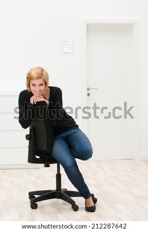 Pretty Young Smiling Woman Sitting on Black Chair at White Room