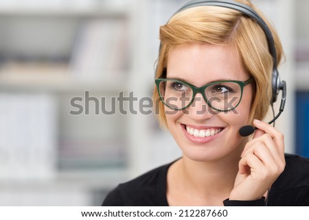 Attractive woman call centre operator wearing heavy framed glasses and a headset smiling as she listens to a conversation with a customer