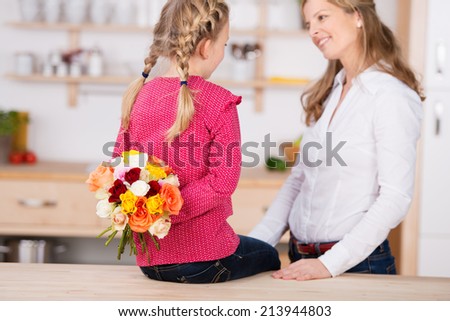 Little girl holding flowers behind her back by her mother on mother\'s day at home