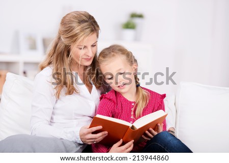 Mother and young daughter reading book on couch at home