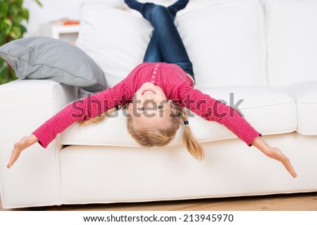 Portrait of a playful girl lying upside down on sofa in the living room