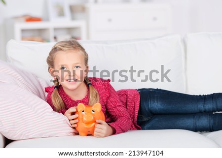 girl lying on sofa holding piggy bank in her hand