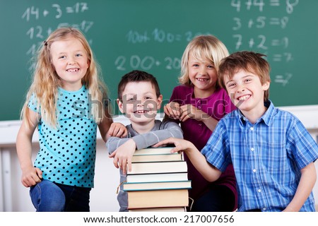 Group of friendly young boys and girls in school with their books piled into a tall stack posing together looking at the camera with happy smiles