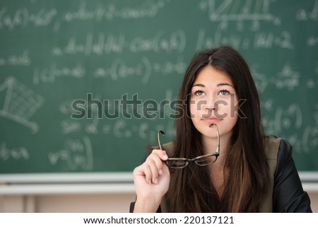 Young woman in class at college or university sitting thinking deeply holding her glasses in her hand as she stares up into the air