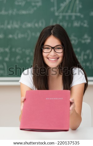 Smiling attractive young college girl holding out a CV in a red file on display to the camera as she prepares to go for a job interview
