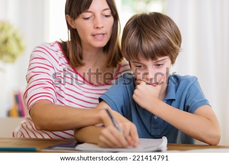 Young mother doing homework with her son pointing to something written in his notebook as he stares thoughtfully at the page