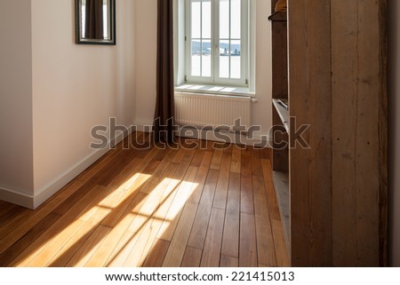 View past a shelving unit of sunlight shining onto a wooden parquet floor through a curtained window