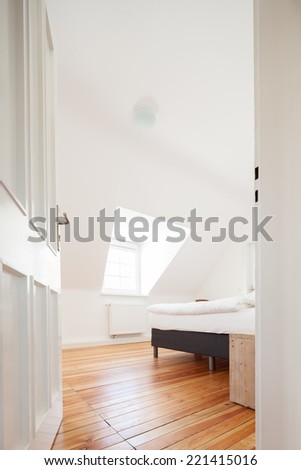 Low angle view through the white painted door into a loft bedroom with a sloping white ceiling, a wooden parquet floor and double bed