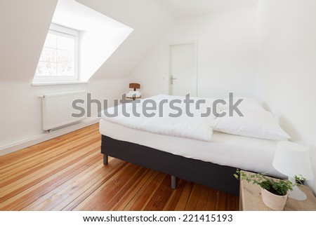 Fresh white modern bedroom interior with a dormer window, wooden parquet floor and double bed