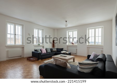 Comfortable modern white lounge or living room interior with large upholstered couches and four bright windows with wood panels and a parquet floor