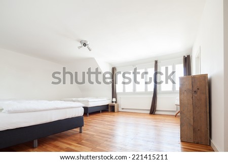 Bright white loft bedroom interior with a row of small windows and two double beds on a wooden parquet floor