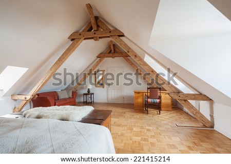 Spacious loft bedroom interior in a roof apex viewed from the bed showing exposed roof timbers, a wooden parquet floor and desk