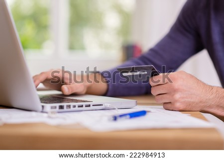 Man making a purchase online entering the details of his credit card onto a laptop computer in an e-commerce concept