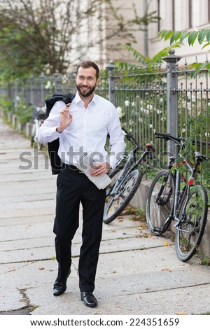 Smiling Handsome Businessman in Black and White Suit Walking on the Street with Coat on Shoulder While Holding Newspaper on Other Hand.