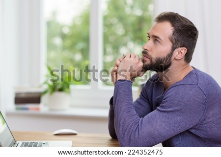 Thoughtful businessman staring into space with his chin resting on his hands as he sits at his desk in the office
