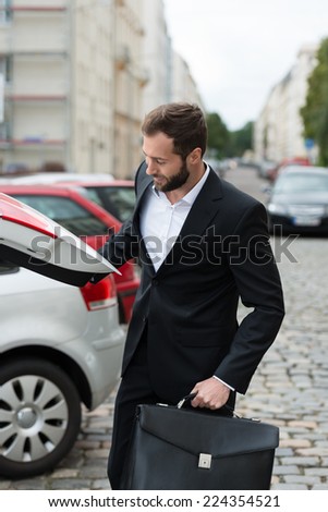 Smiling businessman getting his briefcase from the boot of his car as he arrives at work in the morning