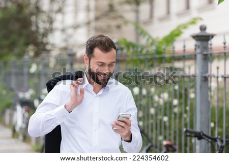 Smiling Handsome Man with Coat on the Shoulder Using Mobile Phone While Walking on the Street